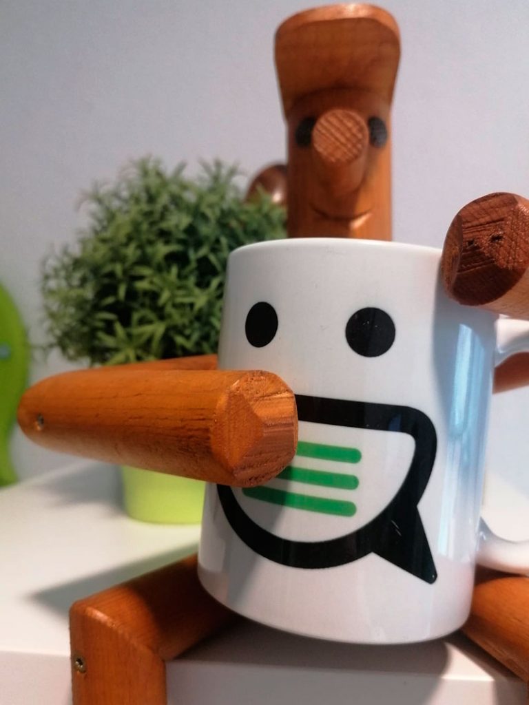 muñeco de madera con una taza con el logo de Haz Marca